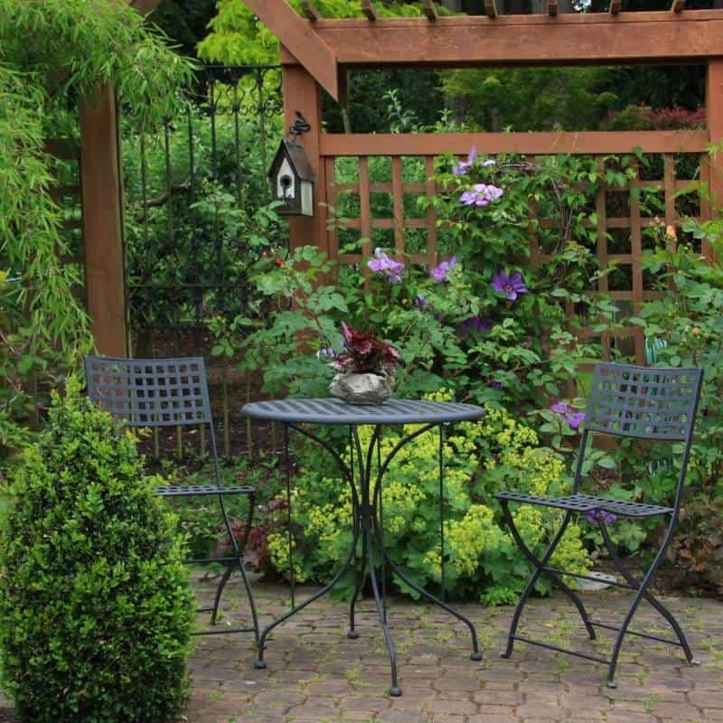 bistro table and chairs in a garden under a wooden arbor