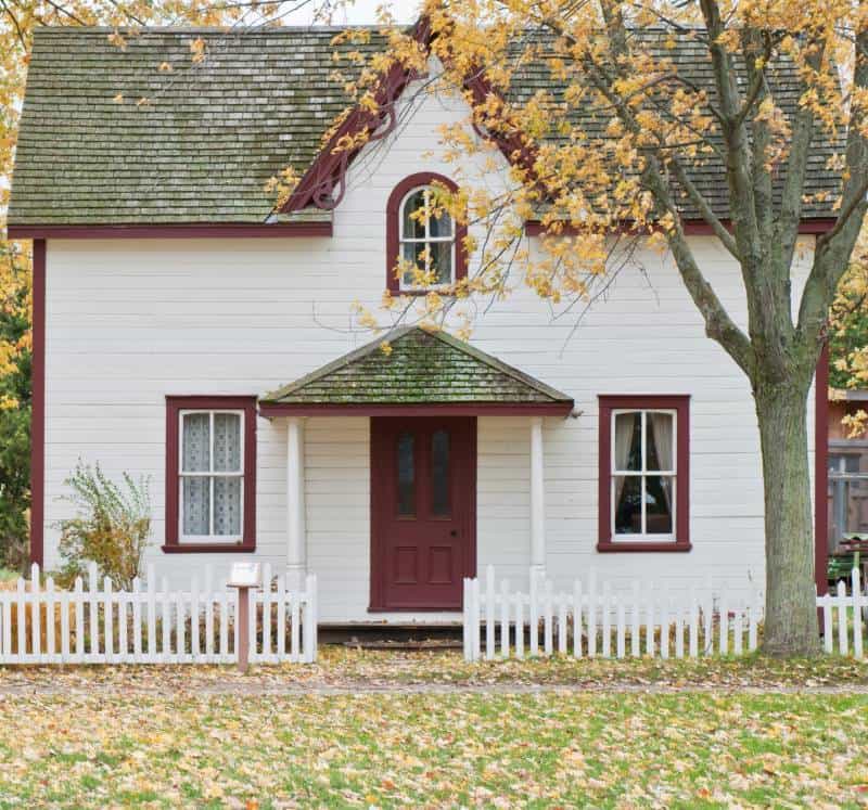 Cape code style home with red trim and low picket fence
