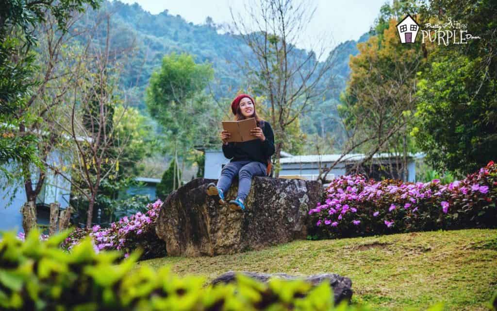 Woman in red sitting on a tree stump with a notebook surrounded by beautiful landscape and water.