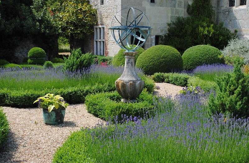 geometric statue surrounded by green hedges and a gravel path
